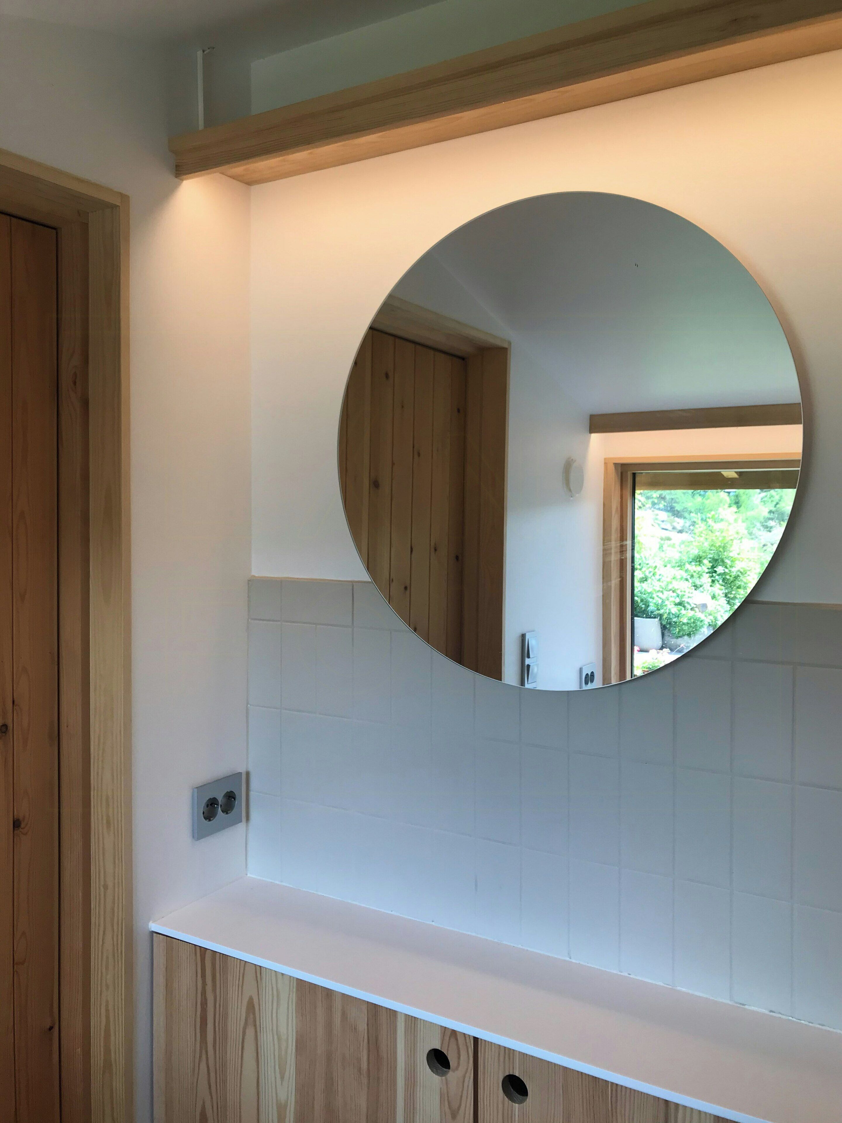 Une salle de bain avec un meuble-lavabo en bois, un miroir rond et une vue sur une porte et une fenêtre.