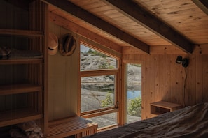 L’intérieur d’un chalet en bois, avec un lit, des étagères et une fenêtre donnant sur un paysage rocheux.