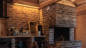 A rustic kitchen with a brick fireplace, wooden beams, and a wooden floor.