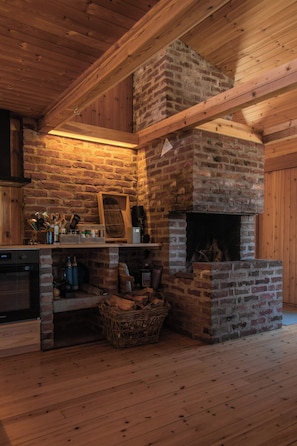 Une cuisine rustique avec une cheminée en briques, des poutres apparentes et un plancher en bois.
