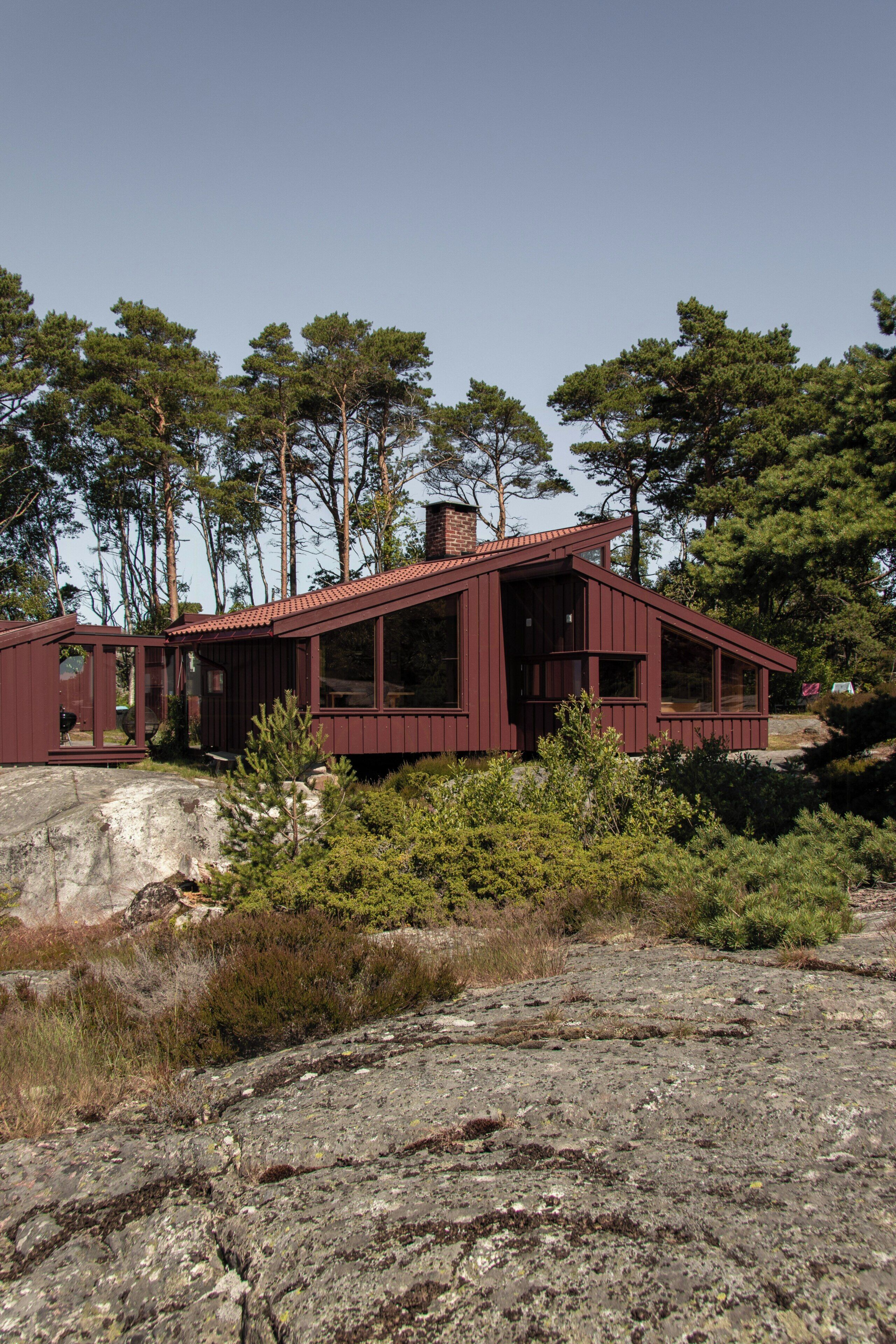 A modern house with a red exterior, surrounded by trees and rocky terrain.