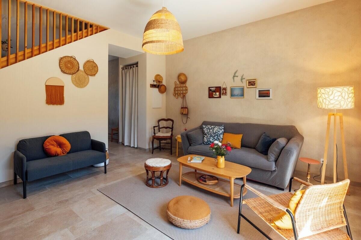 A living room with a sofa, coffee table, and a chair. There is a staircase with wooden railings and a hanging light fixture.