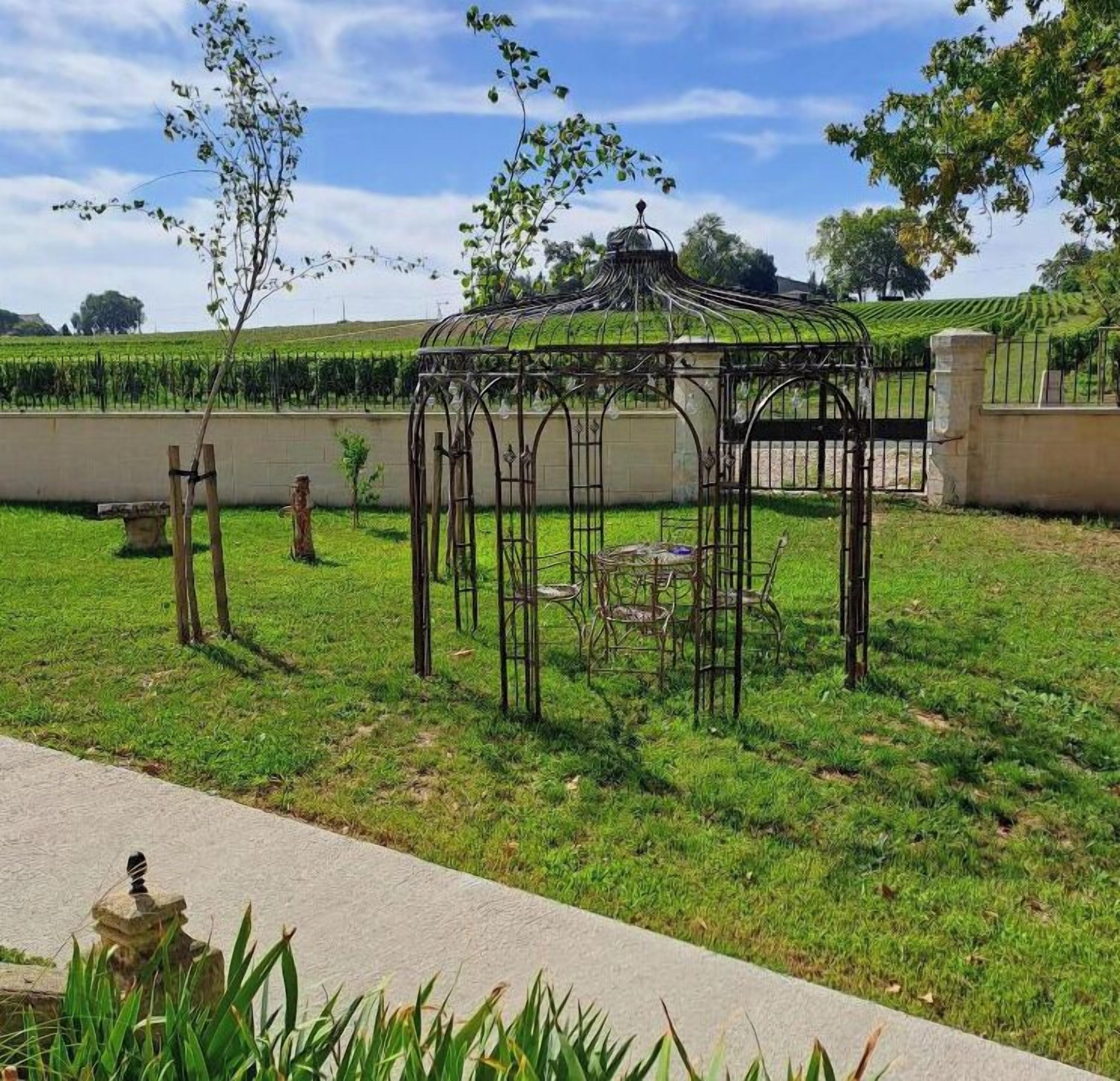 Un jardin agrémenté d’un kiosque en métal, d’un banc et d’une structure en pierre.