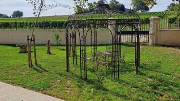 Un jardin agrémenté d’un kiosque en métal, d’un banc et d’une structure en pierre.