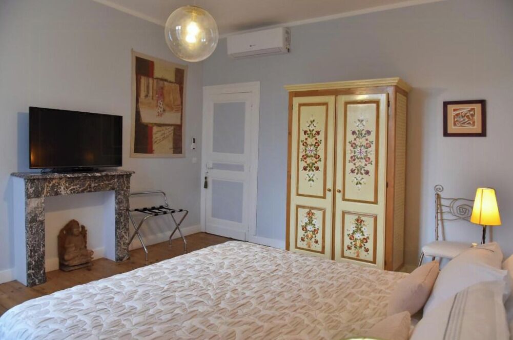 A bedroom with a bed, a television on a stand, a wardrobe, and a lamp.
