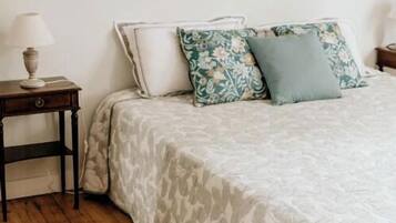 A bedroom with a bed, a nightstand, a lamp, a painting on the wall, and a patterned rug.