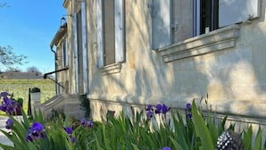 A building with a stone facade, large windows, and a garden with purple flowers.