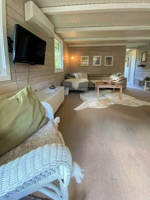 Ein gemütliches Cabin-Interieur mit einer Couch, einem an der Wand befestigten Fernseher und einer Holzbalkendecke.