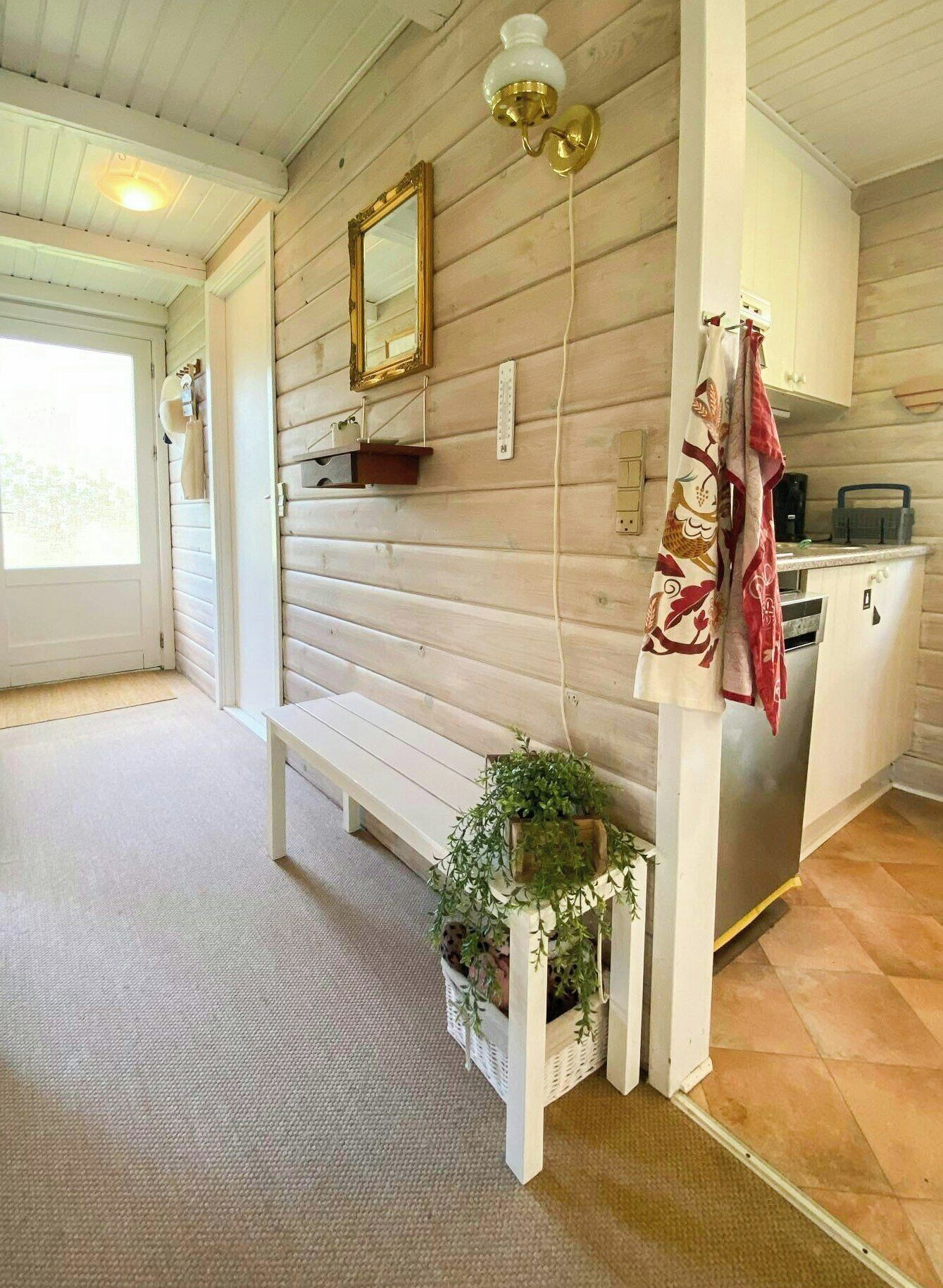 Un intérieur en bois comprenant un banc, un luminaire fixé au mur, un miroir et un coin cuisine.
