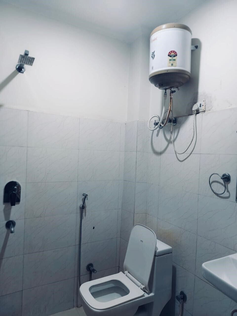 A small bathroom with a toilet, a wall-mounted water heater, and a sink.
