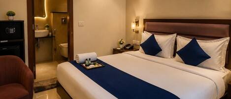 A hotel room with a bed, bedside table, chair, and a bathroom visible through an open door.