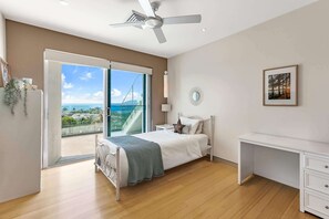 Ein Schlafzimmer mit Bett, Schreibtisch, Deckenventilator, Fenster mit Aussicht und einer Tür zum Balkon.