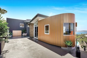 Ein modernes Haus mit einer gewölbten Holzfassade, einer Steinsäule und Blick auf den Ozean.