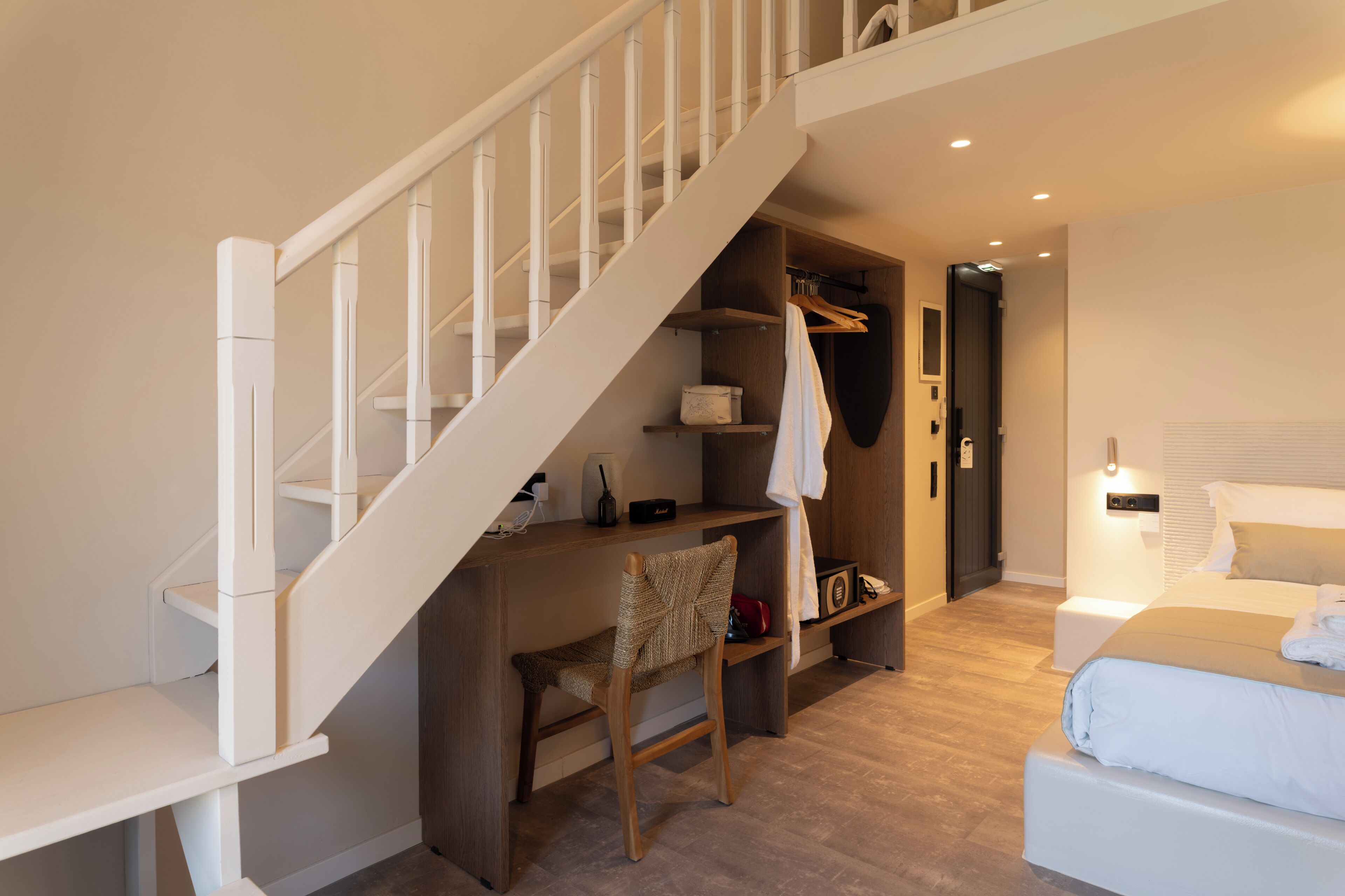 A bedroom with a bed, a desk, a chair, a wardrobe, and a staircase.