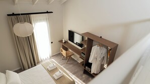 A modern bedroom with a bed, a desk, a TV, and a walk-in closet. - Ichos Apartments (Volissos)