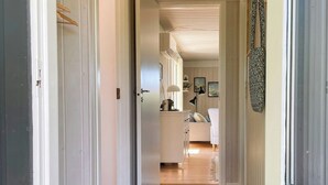 Un couloir avec un paillasson foncé qui mène à une cuisine dotée d’un plan de travail blanc et de placards.