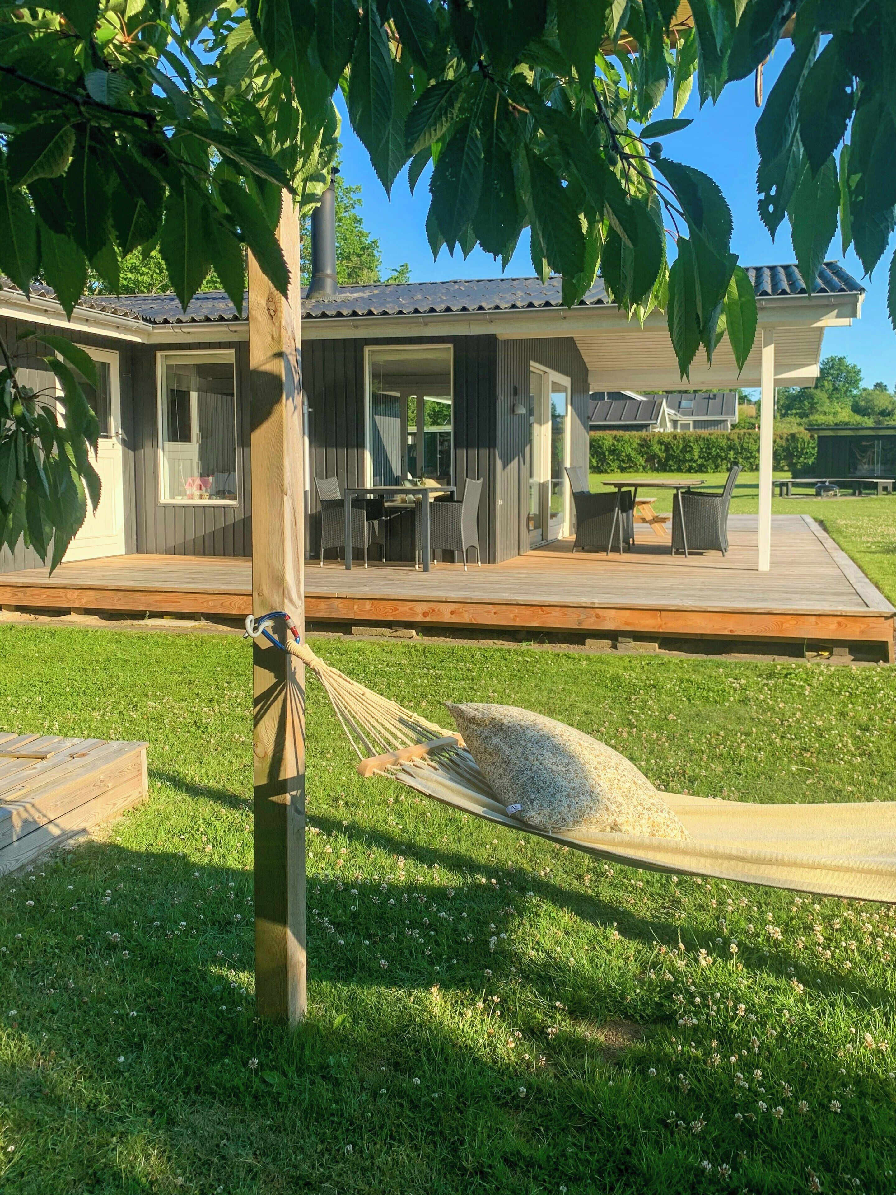 A covered outdoor area with a table and chairs, a hammock, and a grassy lawn.