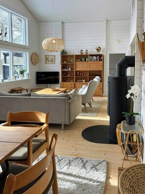 Ein gemütliches Wohnzimmer mit einer Couch, Sesseln, einem Fernseher, Holzregalen und einem Kamin.