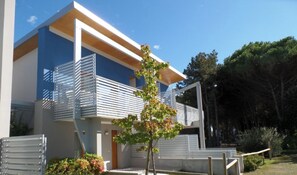 A modern two-story building with a balcony, a small tree, and a clear sky. - Lovely Apartment Surrounded by Greenery in Bibione (San Michele al Tagliamento)