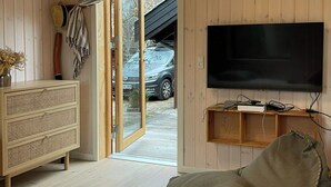 Een gezellige kamer met een houten vloer, een aan de muur bevestigde televisie, een bank, een rieten bijzettafeltje en een deur naar buiten.
