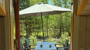 Een open deur die uitkomt op een terras met een tafel, stoelen en een parasol.