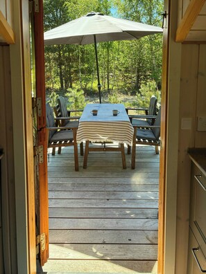 Eine offene Tür, die zu einer Terrasse mit Tisch, Stühlen und Sonnenschirm führt.