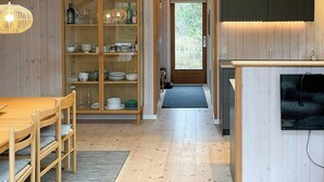 Een moderne keuken met houten kastjes, een eethoek met tafel en stoelen, en uitzicht door de deur.