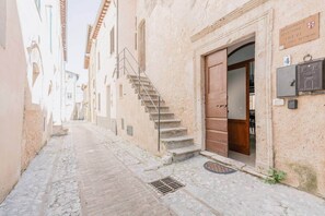 A narrow cobblestone street flanked by historic buildings with a staircase leading to a door.