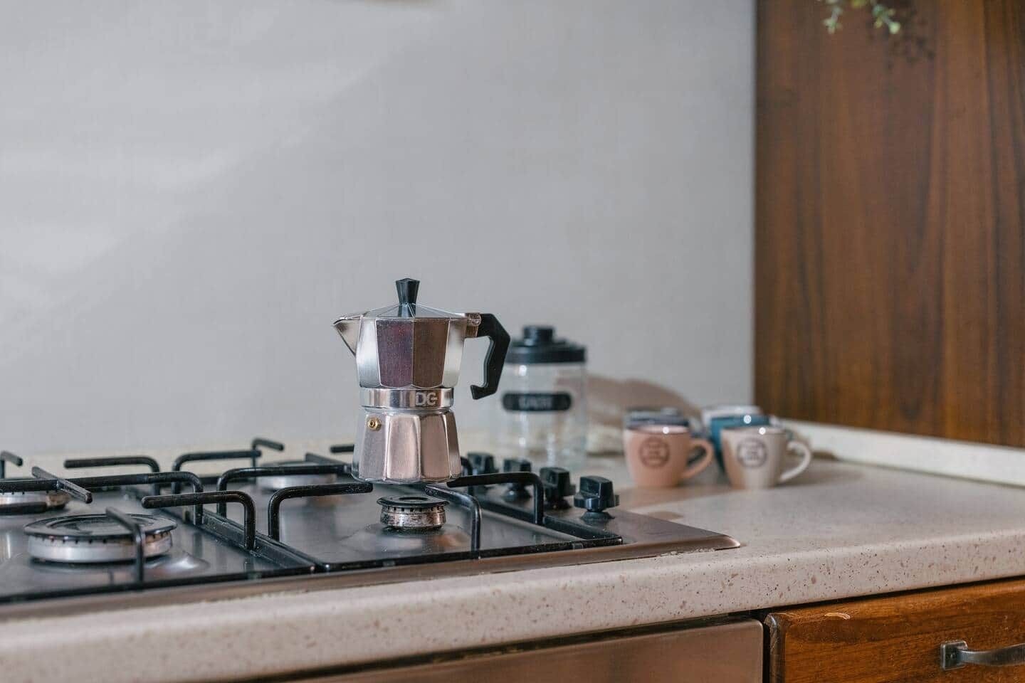 A kitchen with a gas stove, a coffee maker, and two mugs on the counter.