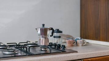 A kitchen with a gas stove, a coffee maker, and two mugs on the counter.