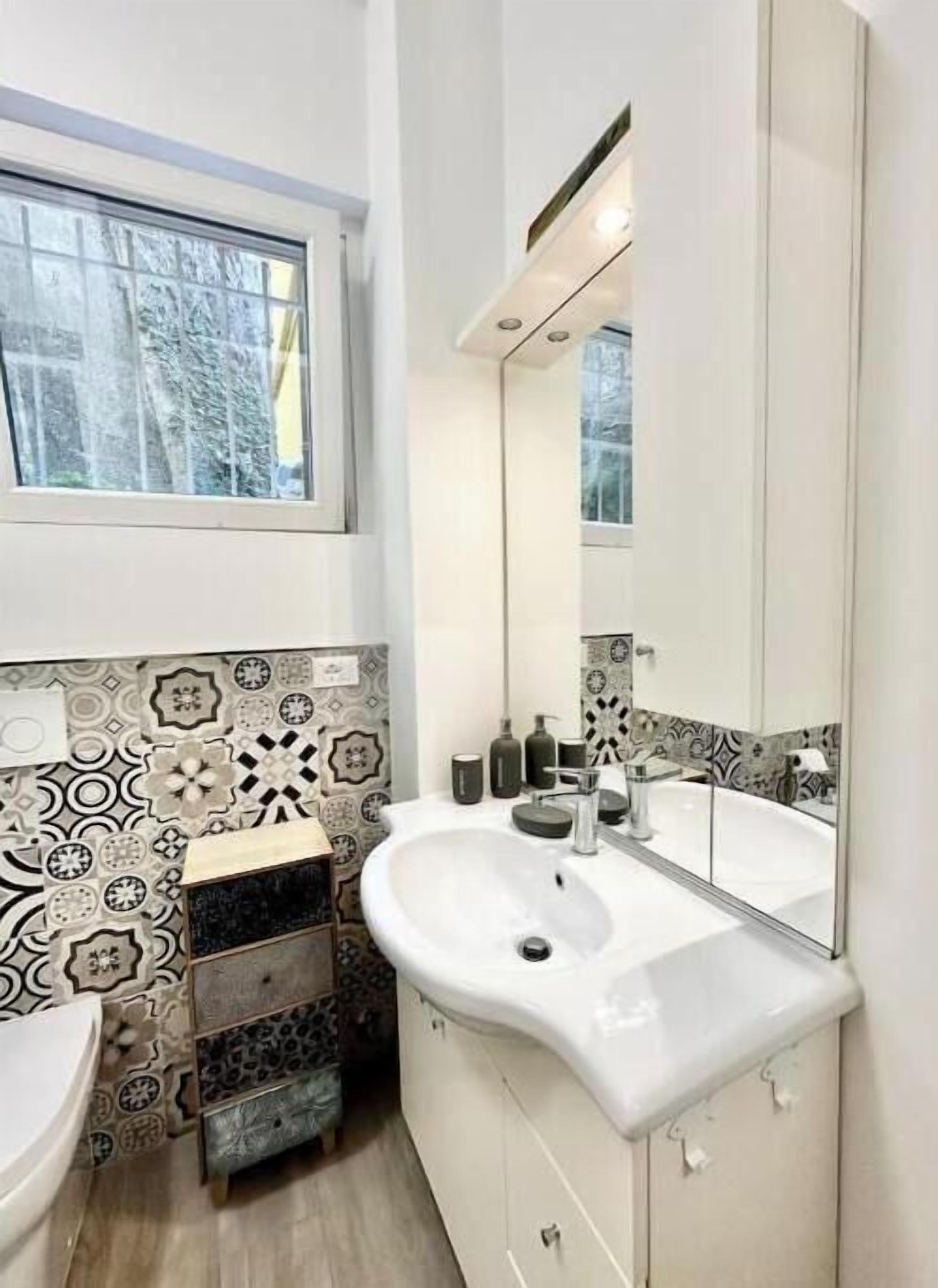 A bathroom with a white sink, a mirror, and patterned tiles.