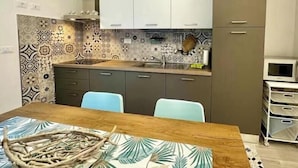 A compact kitchen with a wooden table, two chairs, patterned backsplash, and modern cabinets. - Hostdomus - Garden Suite (Finale Ligure)