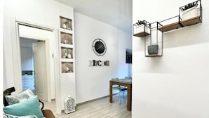 A modern living room with a wooden floor, a dining table, and a wall-mounted shelf with decorative items. - Hostdomus - Garden Suite (Finale Ligure)
