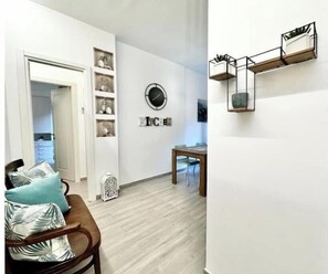 Un salon moderne avec un plancher en bois, une table à manger et une étagère murale agrémentée d’objets décoratifs.