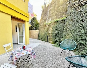 Un patio con tavolo e sedie, un edificio giallo e un muro ricoperto di vegetazione.