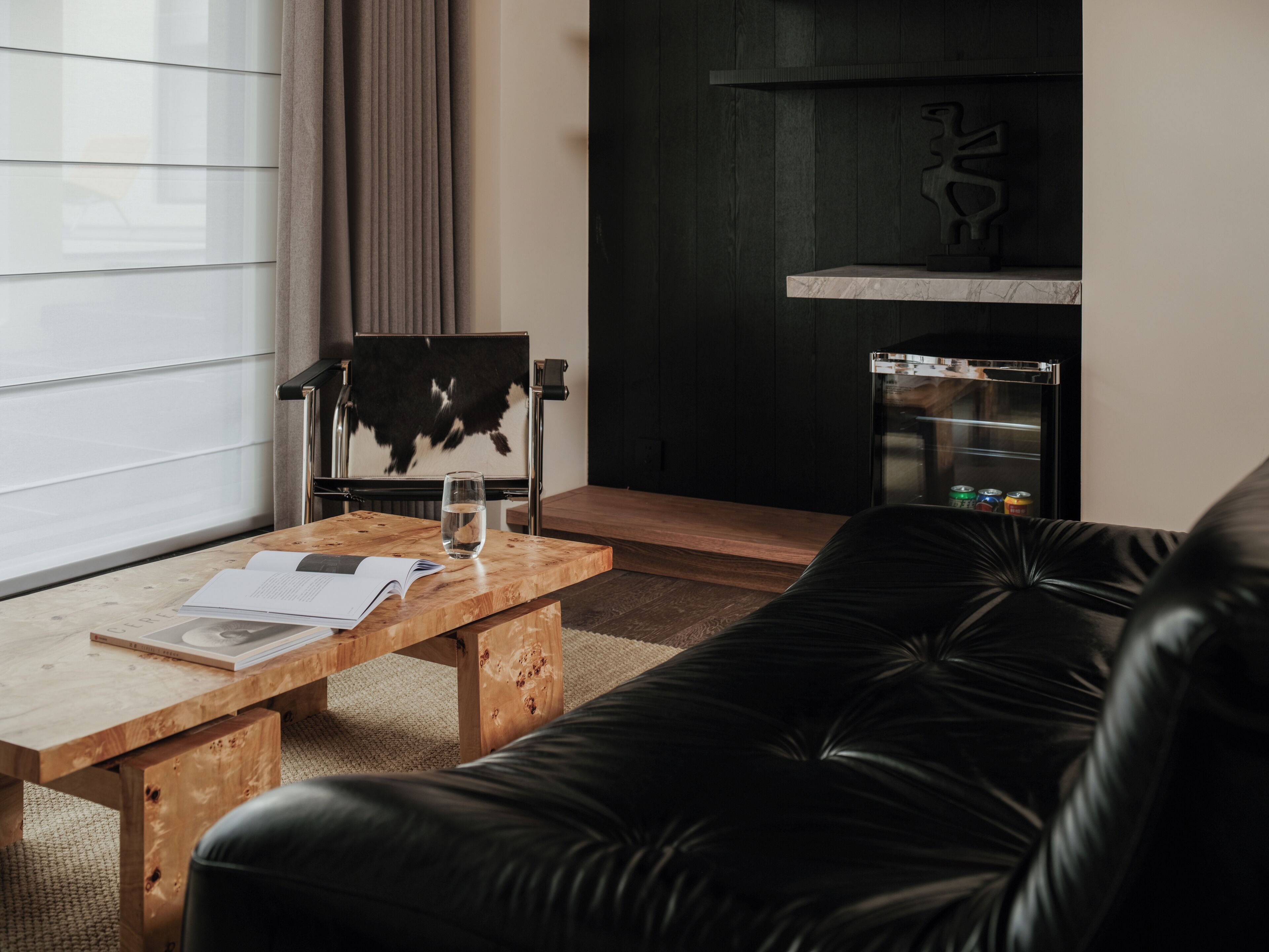 Una sala de estar moderna con una mesa de centro de madera, un sofá de cuero negro, un vaso de agua y una revista.