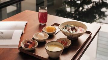 A tray with various bowls of food, a glass of red drink, and a book on a wooden table.