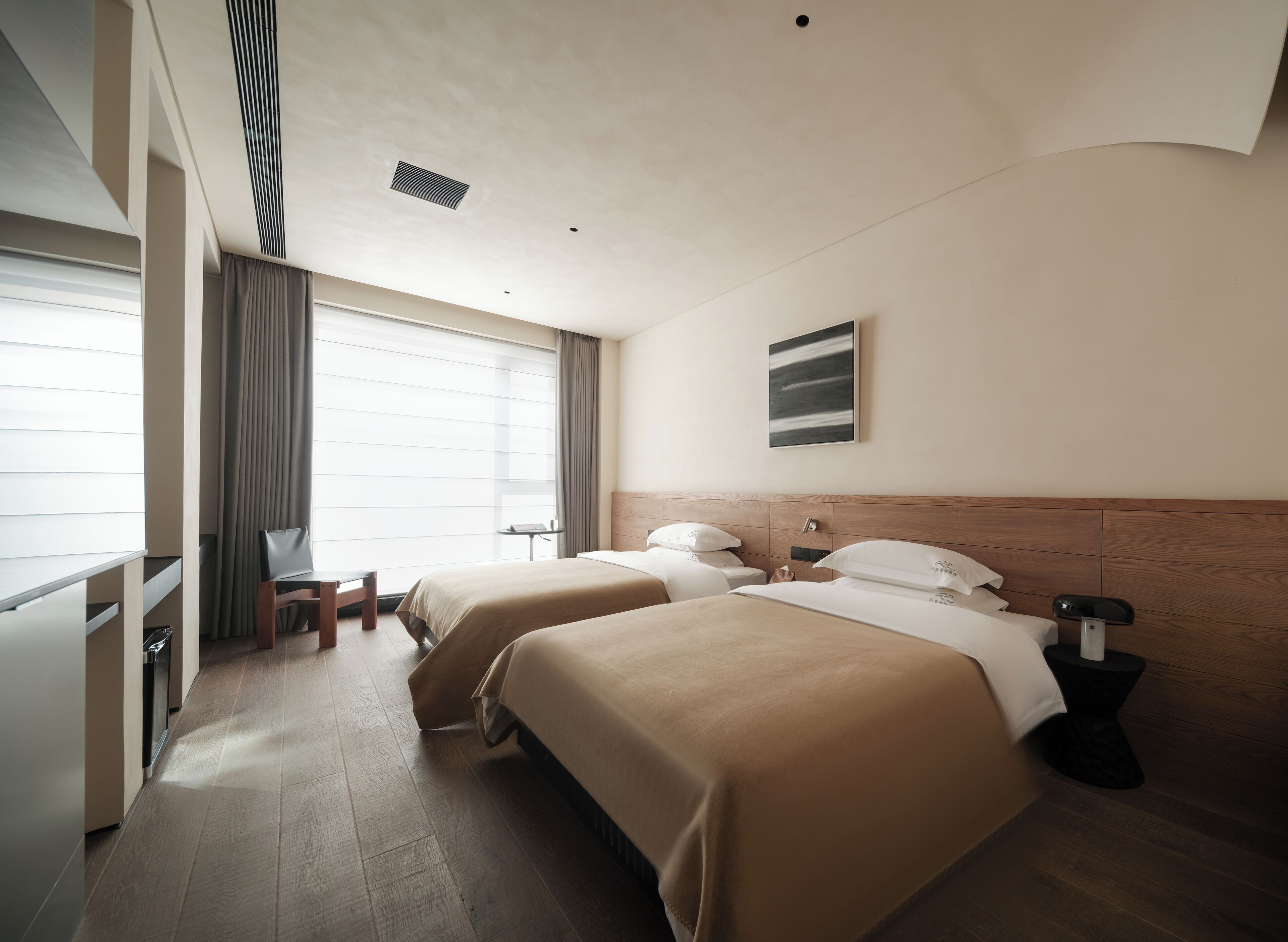 A hotel room with two beds, a desk, a chair, a small table, and a window with curtains.