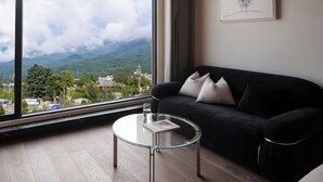 A modern living room with a large window, a black sofa, a glass coffee table, and a framed picture on the wall.