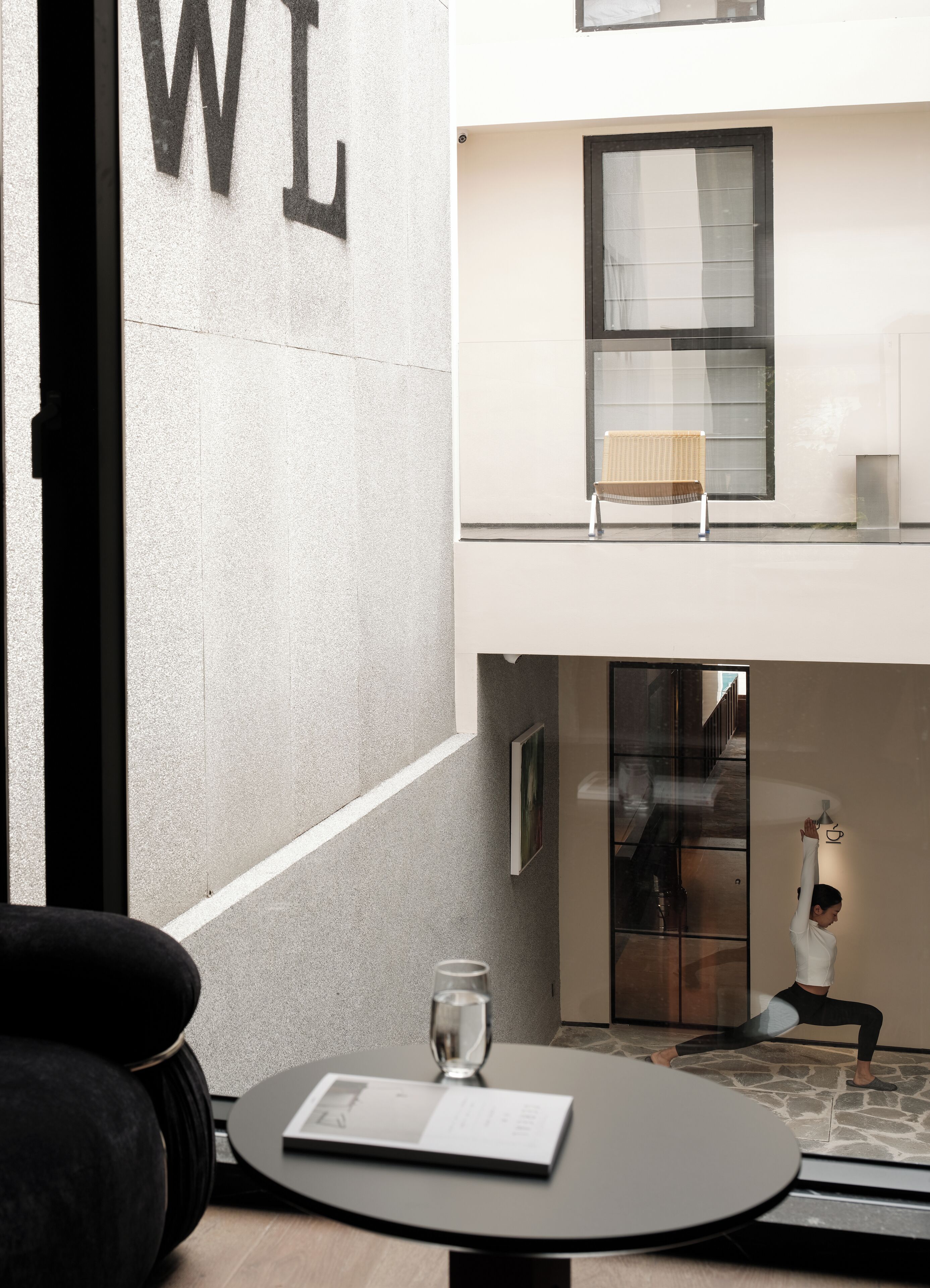 A modern hotel room with a round table, a glass of water, a framed picture, and a view of the building's exterior.