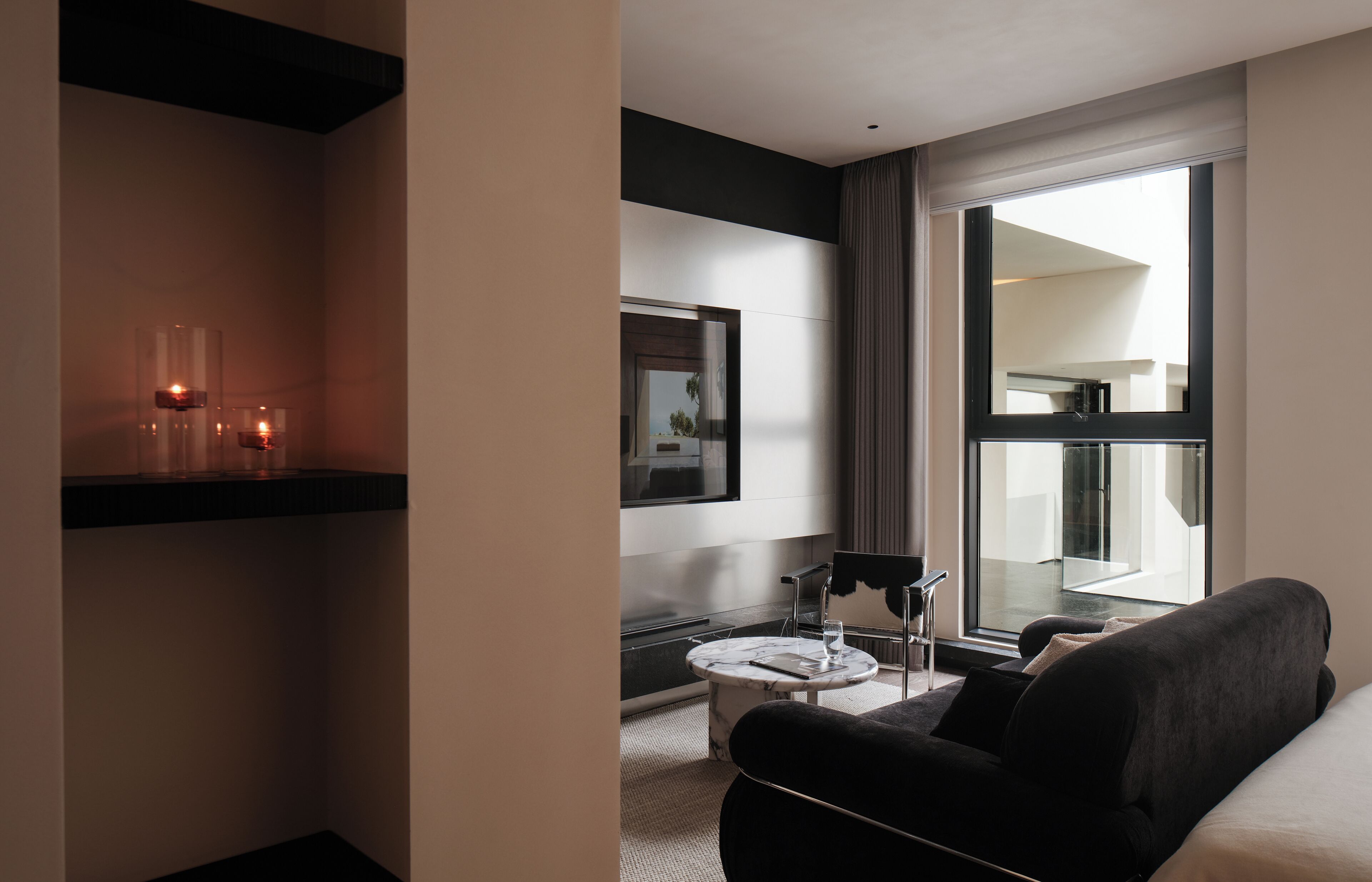 A modern hotel room with a large window, a flat-screen TV, a sofa, and a small table with a glass top.