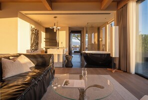 A modern hotel room with a leather sofa, a glass coffee table, a view of a bathroom with a bathtub, and a large window. - Dali Wolan Hidden Luxury Hotel (Dali)