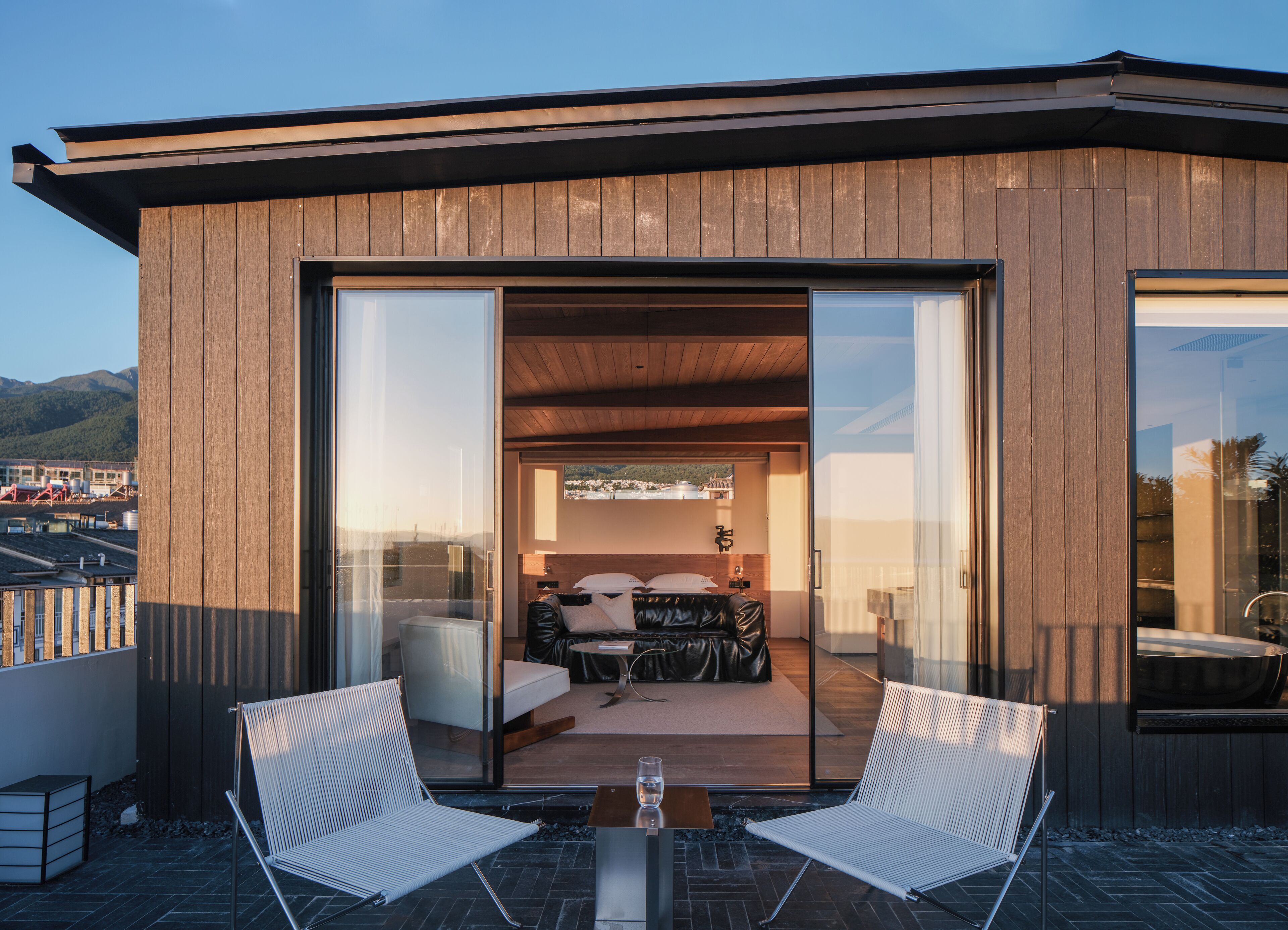 A modern building with a wooden exterior, large sliding glass doors leading to a balcony with two white chairs and a table.