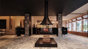 A modern interior with a central fireplace, stone flooring, and large windows.