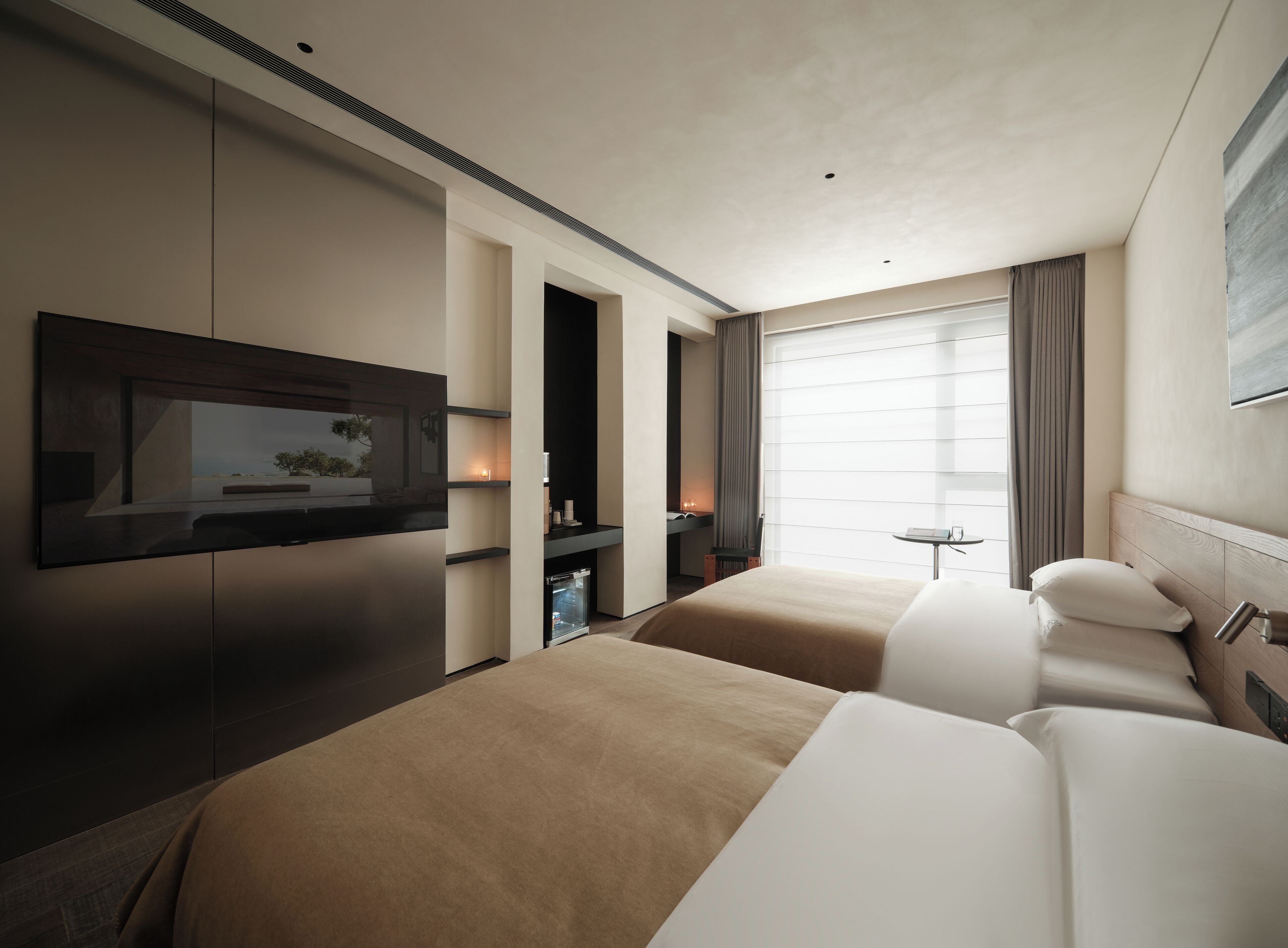 A hotel room with a flat-screen TV, two beds, a small table, and a window with curtains.