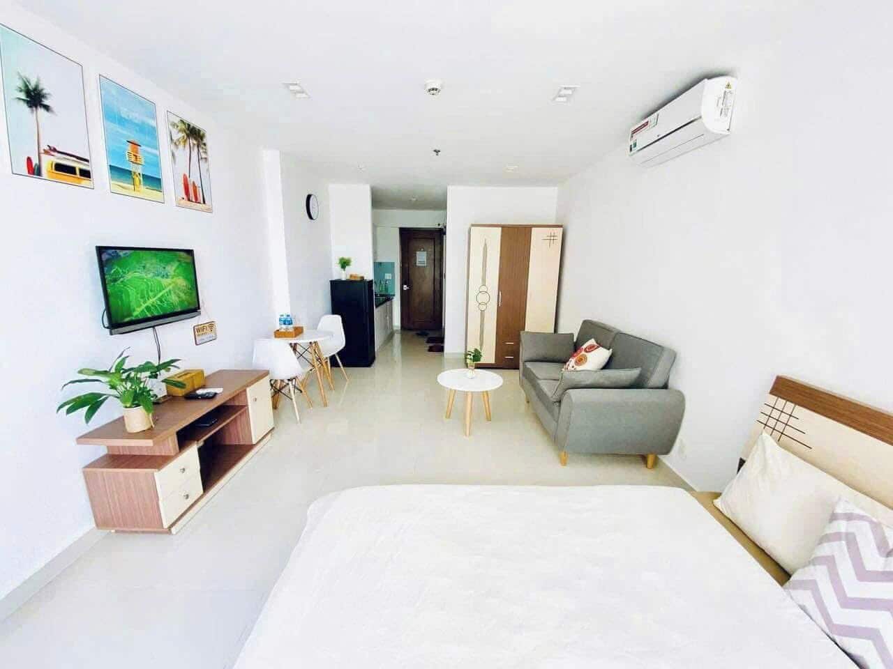 A modern hotel room with a bed, a sofa, a desk with a computer, a TV, and a wall-mounted air conditioner.