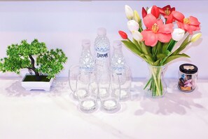 A table with a small artificial tree, multiple water bottles, a vase with flowers, and a container with chocolates. - Apartment near Tan Son Nhat Airport (Tan Son Hoa)