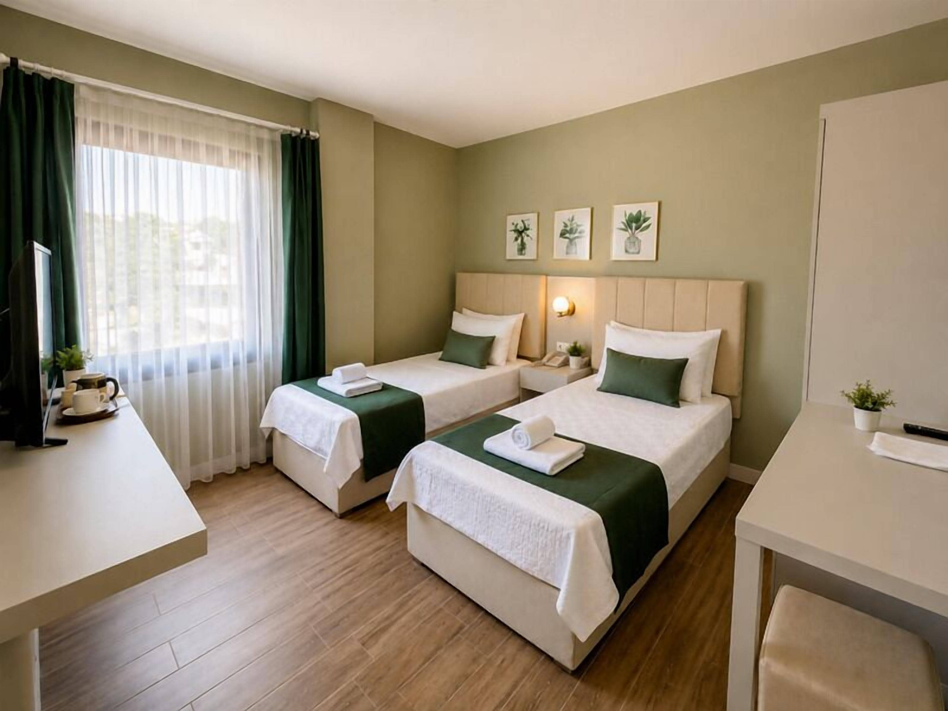 A hotel room with two beds, a desk, a chair, a TV, and a window with curtains.