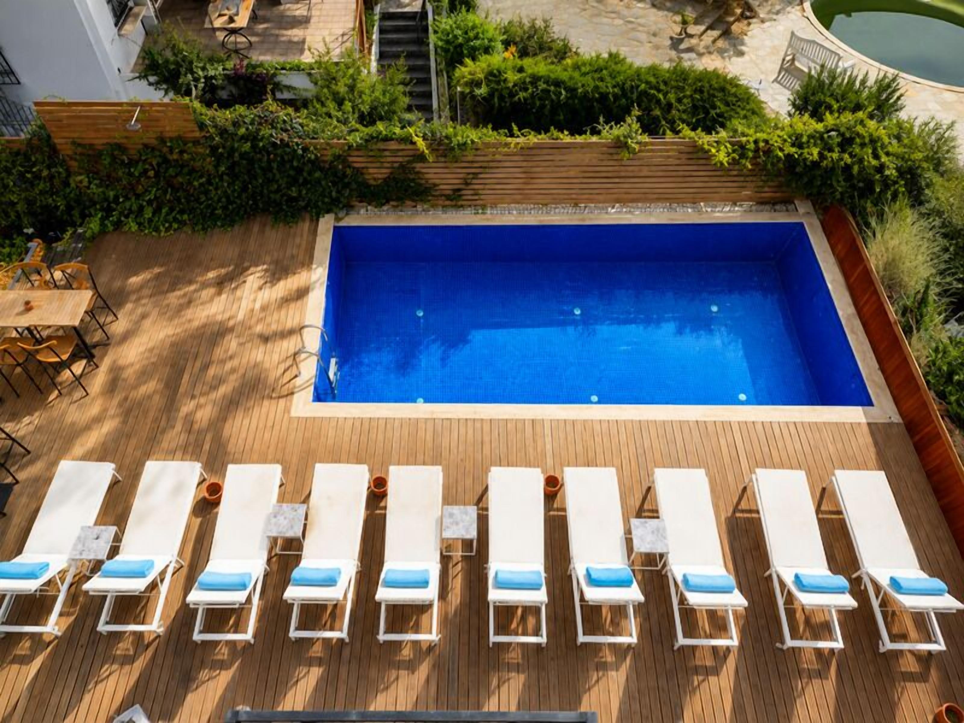 A rectangular swimming pool with a wooden deck and white lounge chairs with blue cushions.
