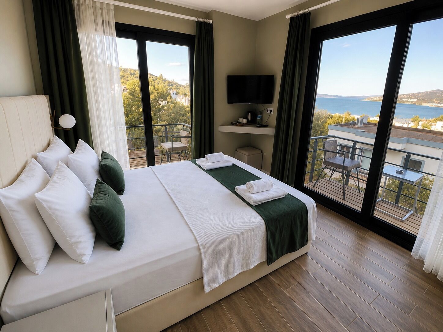 Habitación de hotel con cama, televisor, balcón con mobiliario exterior y vistas al mar.